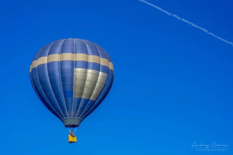 Audrey Cramer Photography's fine art photograph of a blue hot air balloon taking flight in Panguitch Utah with a blue morning sky with contrail