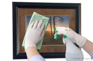 Photo of a person cleaning the glass surface of a framed photograph by Cramer Imaging