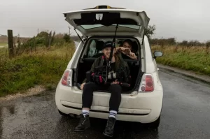 Photograph of a couple men sitting with camera gear in a car trunk