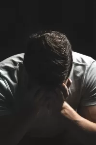 Man holding head while sitting in the dark feeling bad, unhappy, remorseful