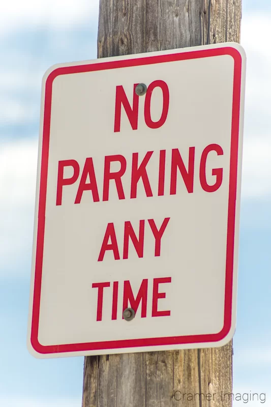 Audrey Cramer Photography's photograph of a "no parking" sign on a telephone pole with blue sky and clouds