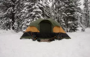 Photograph of a tent set up for winter camping against some pine trees in the snow