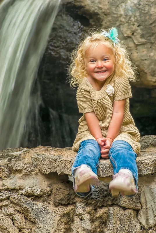 Portrait of a young girl sitting next to a waterfall kicking her legs excitedly