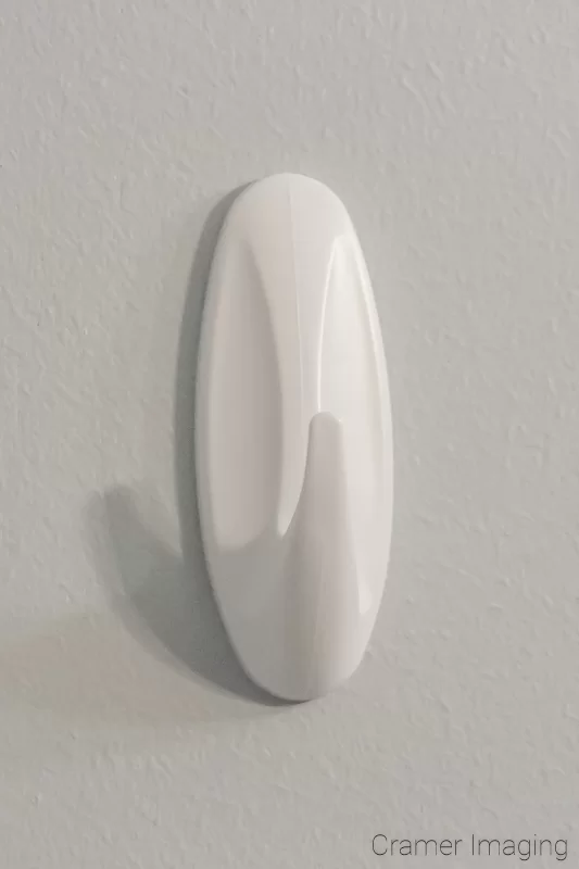 Photograph of a command strip brand white wall hook hanging on the white wall background by Audrey Cramer Photography