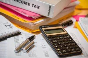 Photo of a calculator and pen sitting on top of a pile of bills and taxes