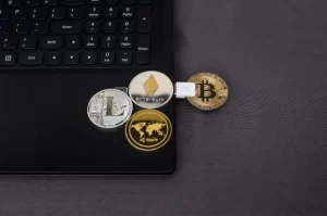 Photograph of a laptop computer and 4 token representing cryptocurrencies collectively representing a digital wallet