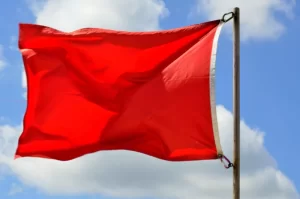 Photograph of a red flag waving against a partly cloudy blue sky