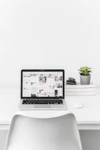 Laptop computer sitting on a desk with a chair while displaying Pinterest on the screen