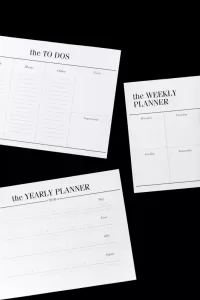 Photograph of a to-do list, a weekly planner and a yearly planner on a black background