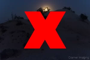 Raw photograph of an underexposed landscape lit by the moon with a red x through the middle