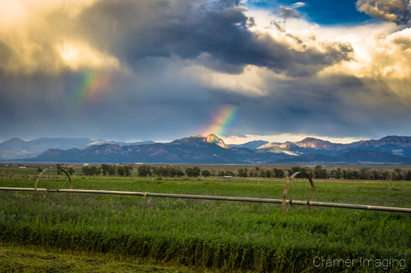 Cramer Imaging's fine art landscape photograph of double rainbow arc appearing in dramatic skies over a growing farm field with wheel lines in Panguitch, Utah