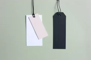 Photograph of 3 tags, one pink tag, one white tag, one black tag, hanging against a green background