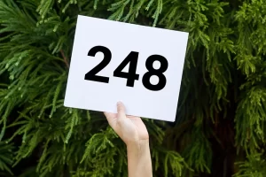 Photograph of a person holding a bidding number against an evergreen background