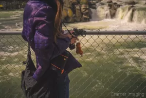 Photograph of professional landscape photographer Audrey holding a camera by a waterfall by Cramer Imaging