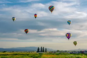 Cramer Imaging's fine art photograph of a hot air balloon cluster taking flight over a field in Panguitch Utah with a blue partly cloudy sky