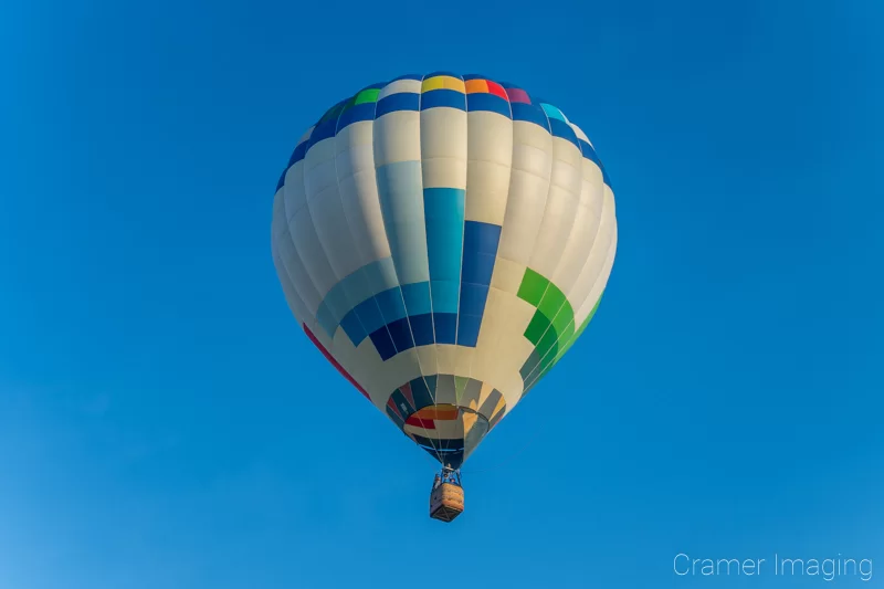 Audrey Cramer Photography's fine art photograph of a white and multi-colored hot air balloon floating over a field in Panguitch Utah with a blue sky