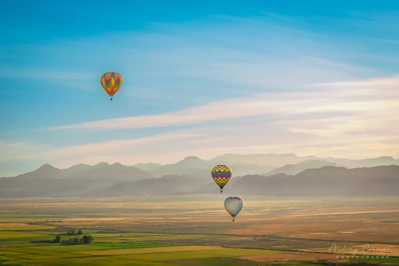 Audrey Cramer Photography's fine art aerial photograph of three hot air balloons flying over a field in Panguitch Utah with a blue partly cloudy sky