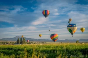 Cramer Imaging's fine art photograph of a hot air balloon cluster floating over a field in Panguitch Utah with a blue partly cloudy sky