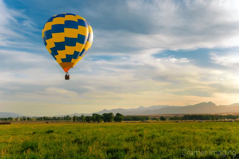 Audrey Cramer Photography's fine art photograph of a yellow and blue hot air balloon taking flight in Panguitch Utah with a blue partly cloudy sky