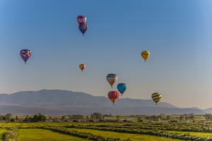 Cramer Imaging's fine art photograph of lots of hot air balloons taking flight in Panguitch Utah over a farm field and mountains