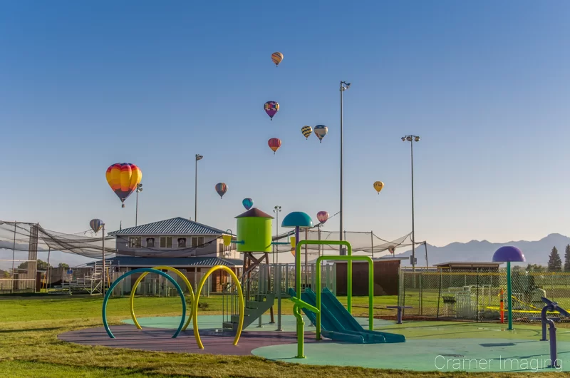 Audrey Cramer Photography's fine art photograph of lots of hot air balloons taking flight in Panguitch Utah over playground equipment and a baseball field