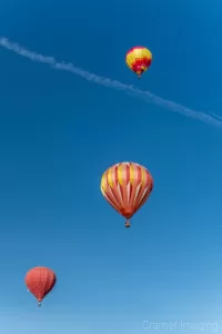 Cramer Imaging's fine art photograph of three colorful hot air balloons taking flight in Panguitch Utah with a blue morning sky with contrail