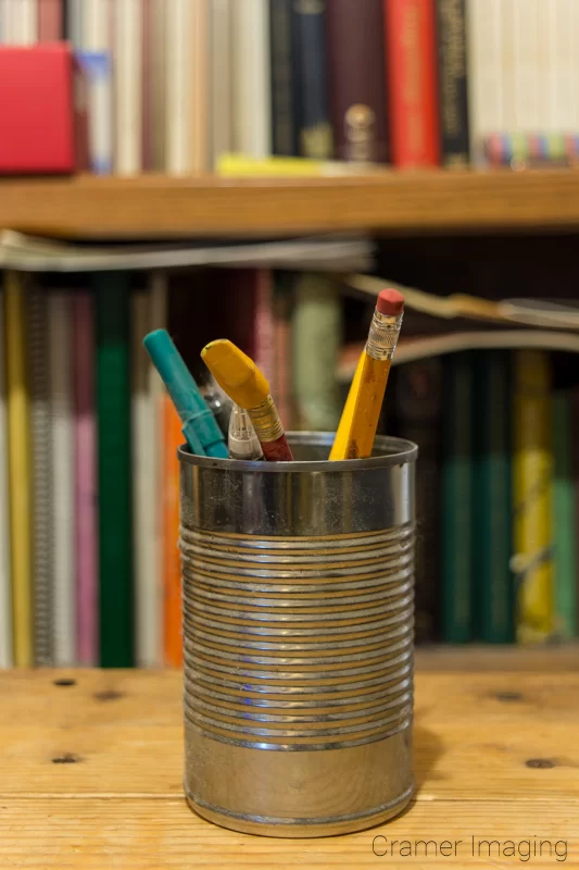 Audrey Cramer Photography's photograph of a can with pencils and a bookshelf demonstrating bokeh