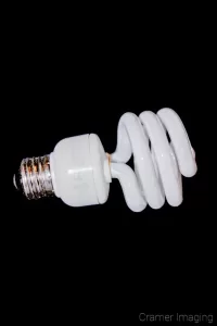 Photograph of a single compact fluorescent light bulb on its side on a black background by Cramer Imaging