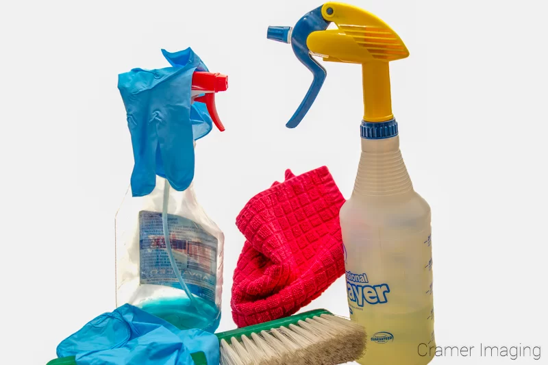 Audrey Cramer Photography's photograph of cleaning chemicals in spray bottles, disposable blue gloves, a red rag, and a duster