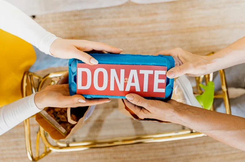 Photograph of hands holding donations with a sign saying 'donate'