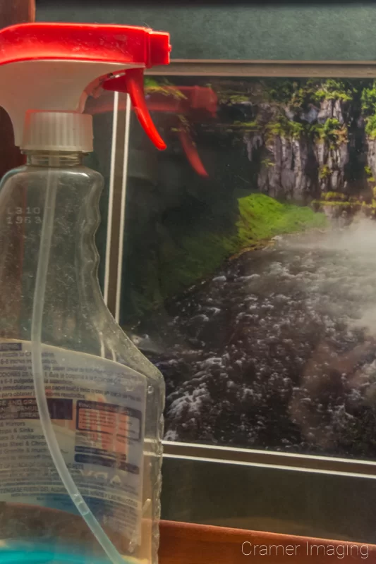 Photograph of a framed landscape photo behind glass with glass cleaner for removing fingerprints by Audrey Cramer Photography