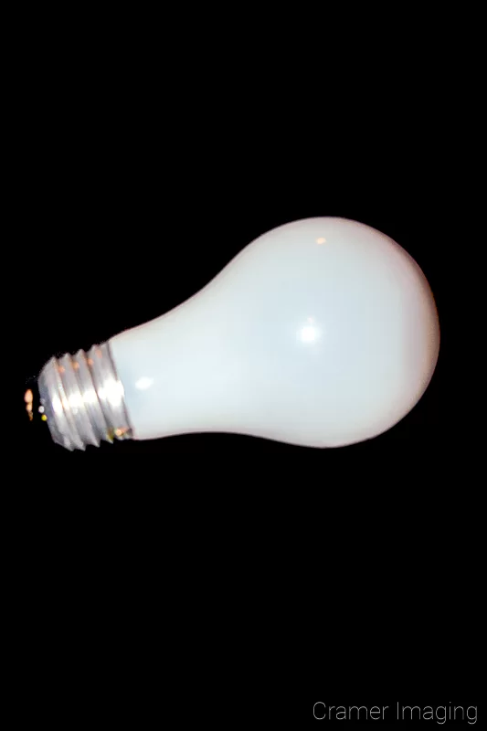 Photograph of a single incandescent light bulb on its side on a black background by Audrey Cramer Photography