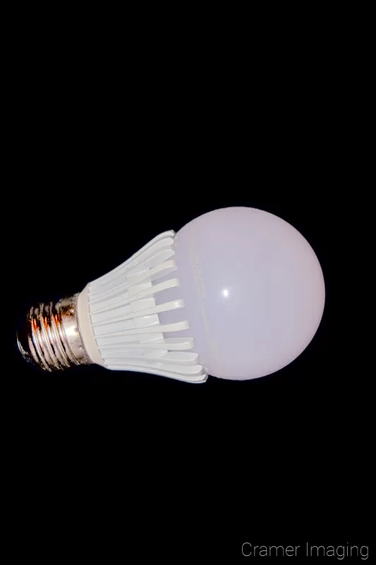 Photograph of a single LED light bulb on its side on a black background by Audrey Cramer Photography