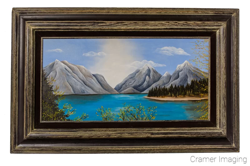 Audrey Cramer Photography's photograph of a framed landscape painting with mountains and a lake on a white wall