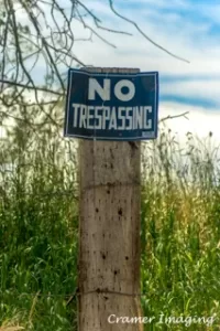 Cramer Imaging's photograph of an old "no trespassing" sign on a fence post with grass