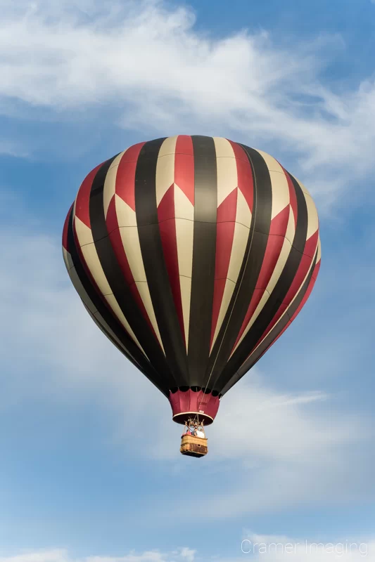 Cramer Imaging's fine art photograph of one tri-color rainbow hot air balloon taking flight in Panguitch Utah with a blue partly cloudy sky