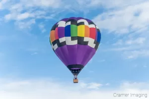 Cramer Imaging's fine art photograph of one purple rainbow hot air balloon taking flight in Panguitch Utah with a blue partly cloudy sky