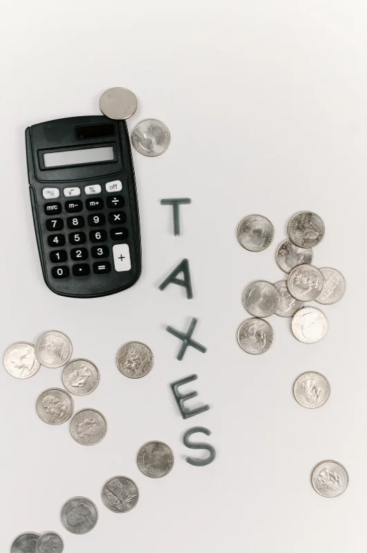 Photograph of the word 'taxes' with a simple black calculator and several dimes scattered