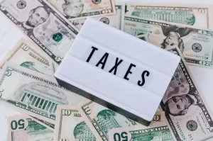 Photograph of a sign saying "taxes" sitting on a pile of US dollars