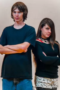 Portrait of a teenaged boy and girl standing back to back with arms crossed