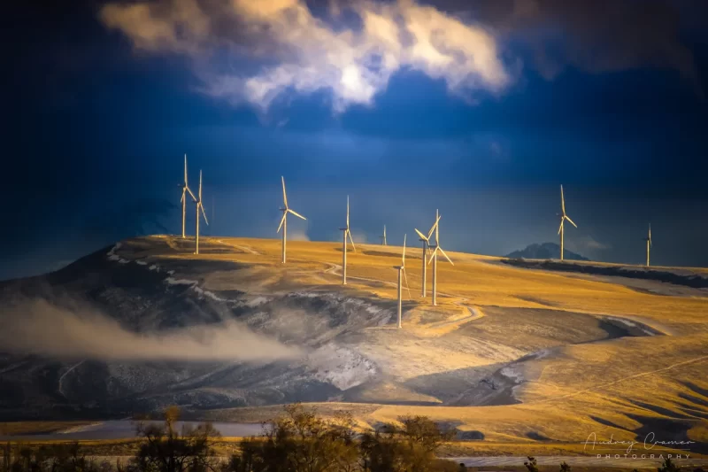 Audrey Cramer Photography's fine art landscape photograph of wind turbines on hill in golden light of sunset just after winter snowstorm