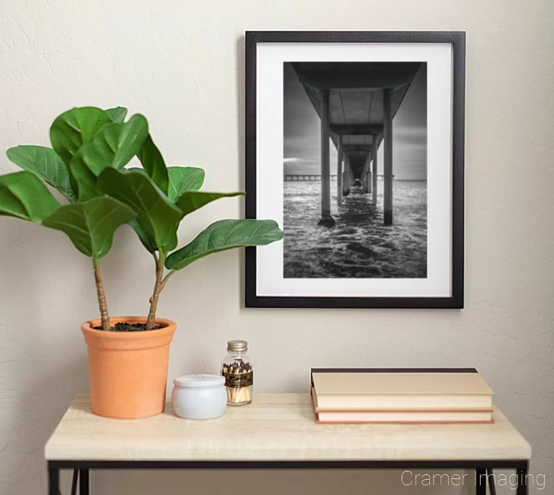 Photograph of Audrey Cramer Photography's fine art photograph 'San Diego Pier' on the wall of a room with a desk and a fake plant