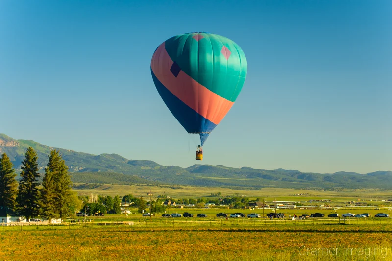 Fine art photograph of a tri-colored hot air balloon soaring over a farm field in Panguitch, Utah by Audrey Cramer Photography