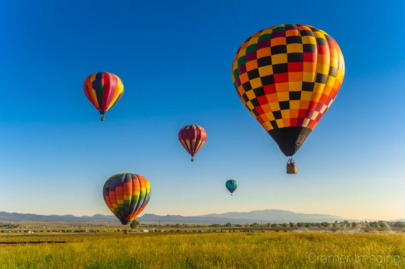 Fine art photograph of a small cluster of hot air balloons flying over a farm field in Panguitch, Utah by Audrey Cramer Photography