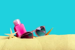 Photograph of sunglasses, bottle of sunscreen, and starfish in the sand