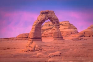 Cramer Imaging's fine art landscape photograph of a cotton candy pink sunset behind Delicate Arch at Arches National Park, Utah