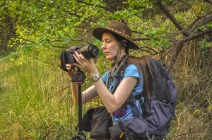 Landscape photographer Audrey Cramer changing lenses on her camera in a forest