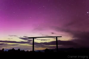 Cramer Imaging's fine art astrophotography photograph of an aurora borealis appearing in the night sky with clouds over a cattle gate silhouette