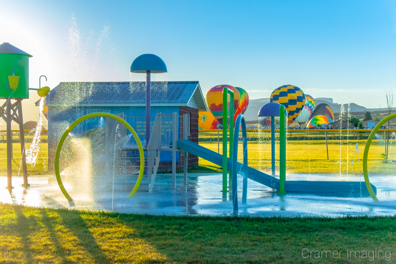 Audrey Cramer Photography's fine art photo of an active splash pad with hot air balloons in the background