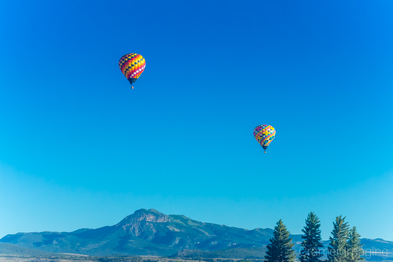 Audrey Cramer Photography's fine art photo of 2 hot air balloons flying in the sky with mountains and trees